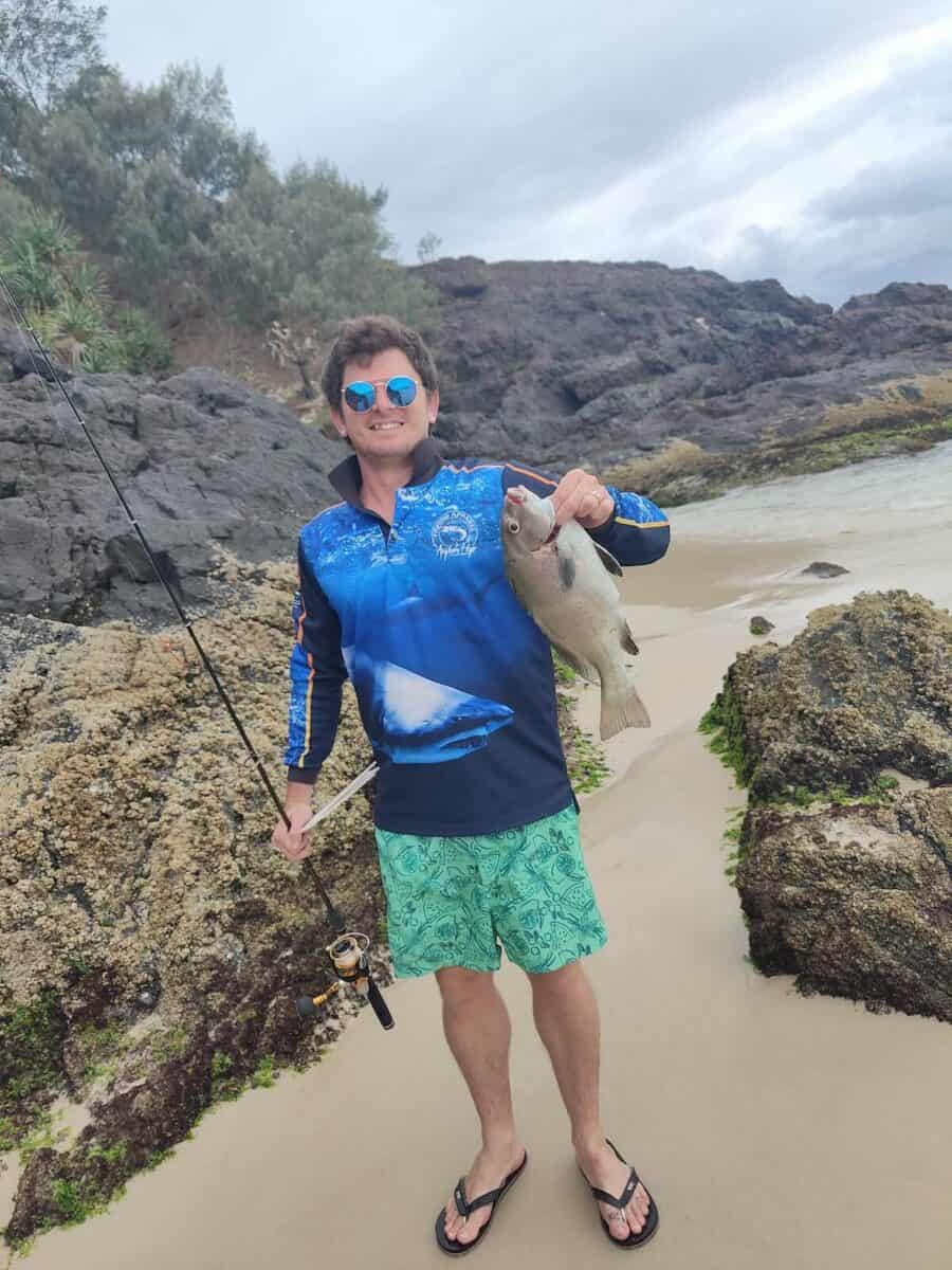 man on beach with fish and rod