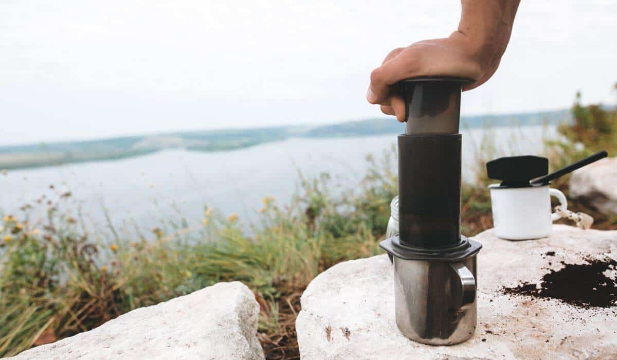 Man using Aeorpress coffee maker near a lake