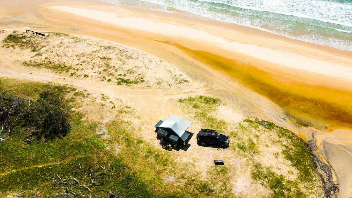 drone view of 4wd and pop up camper on beach in fraser island. 