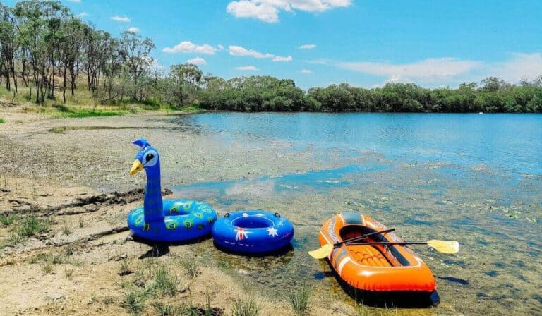 pool floats and kayak next to a river at campsite.