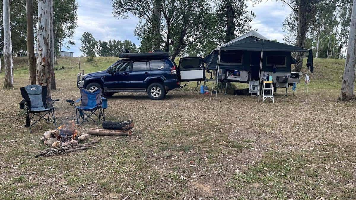 car and camper trailer set up at campsite with camp chairs near fire pit.