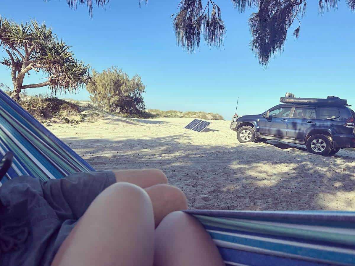 two people sitting in hammock facing a beach campsite with car