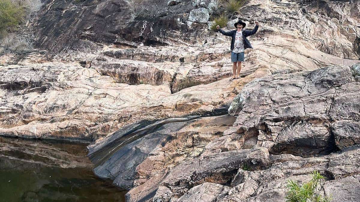 man standing of edge of waterhole near utopia falls in queensland